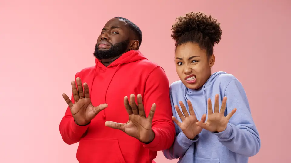 A man and a woman make cringy faces and hold their hands out.
